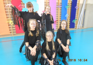 Pięć uczennic w czarnych strojach z czarnymi skrzydłami i pomalowanymi na kolorowo twarzami pozuje do zdjęcia.